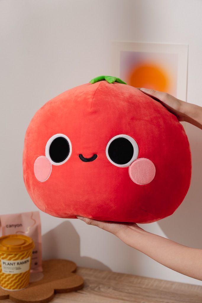 a person holding a red stuffed toy with eyes and nose on it's face