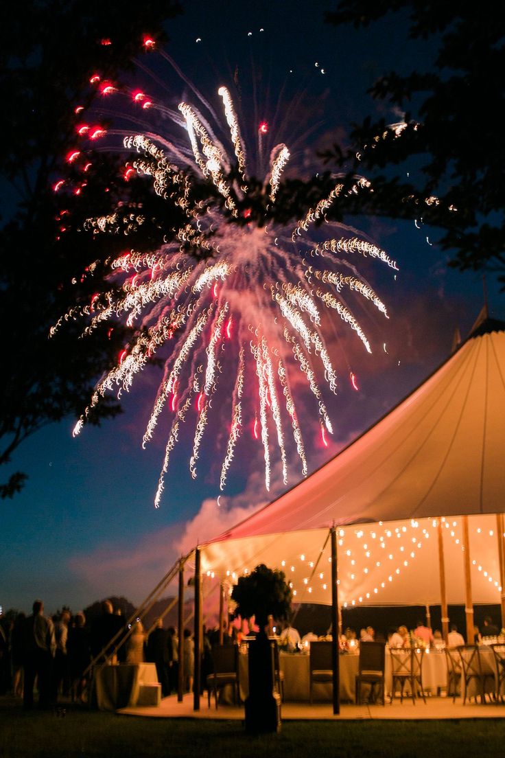 fireworks are lit up in the night sky above a tent with tables and chairs under it