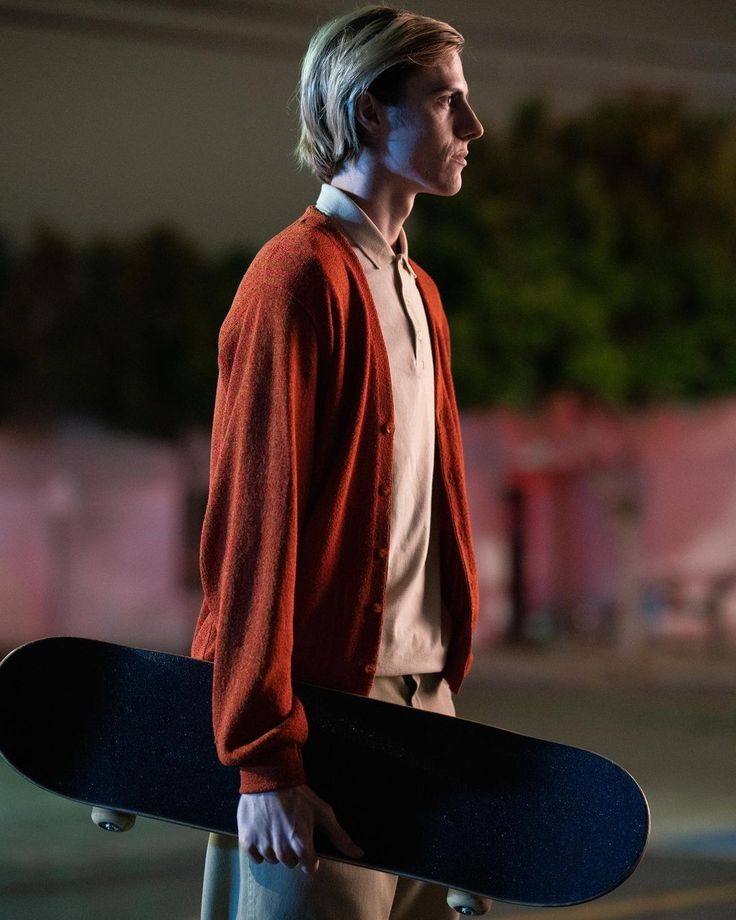 a young man holding a skateboard in his right hand and looking off into the distance