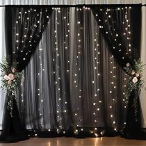 two black vases with white flowers are on the floor in front of a curtain