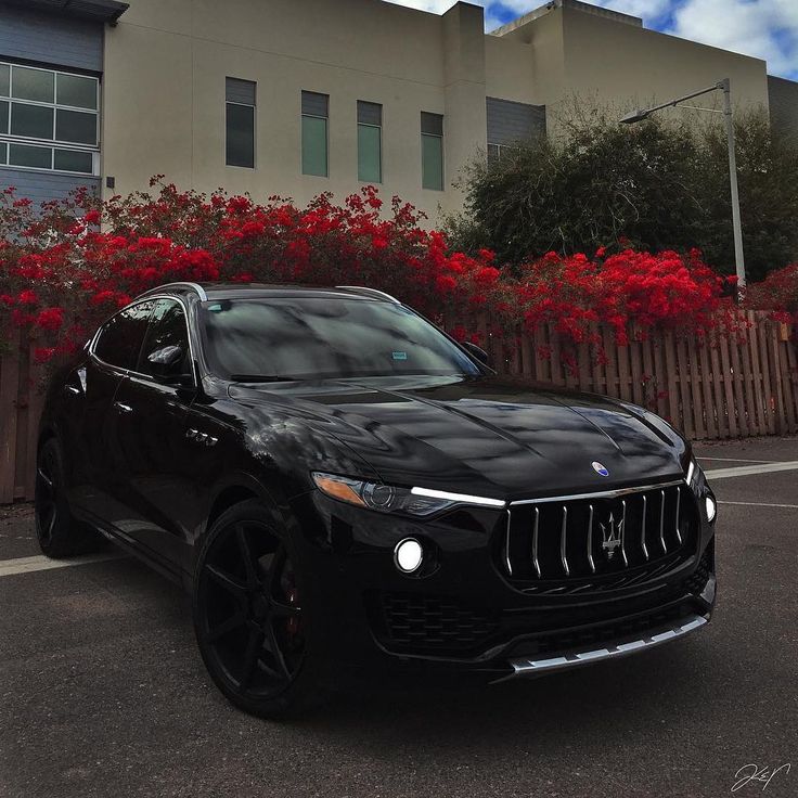 a black masera parked in front of a building with red flowers on the side