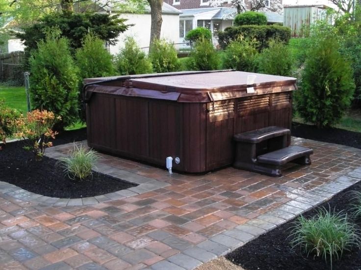 a hot tub sitting in the middle of a brick walkway next to a lush green yard