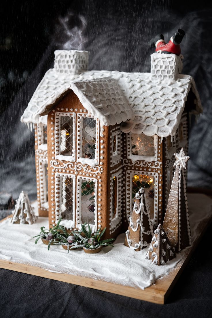 a gingerbread house is decorated with icing and christmas decorations on the roof, while snow falls around it