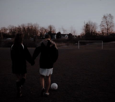 two people holding hands walking towards a soccer ball