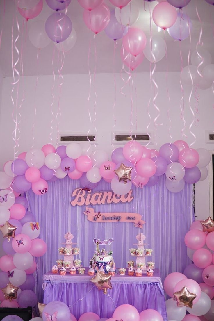 a table topped with lots of pink and purple balloons next to a wall covered in stars