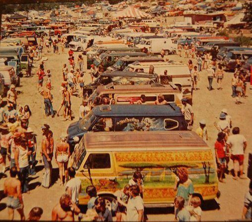 a large group of people standing around parked cars and vans in a parking lot next to each other