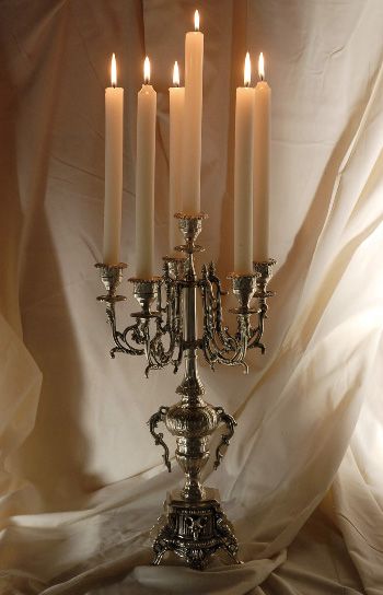 a silver candelabra with five lit candles in it on a white cloth