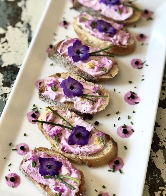 there is a long white plate with bread and purple flowers on it that are sitting on a table