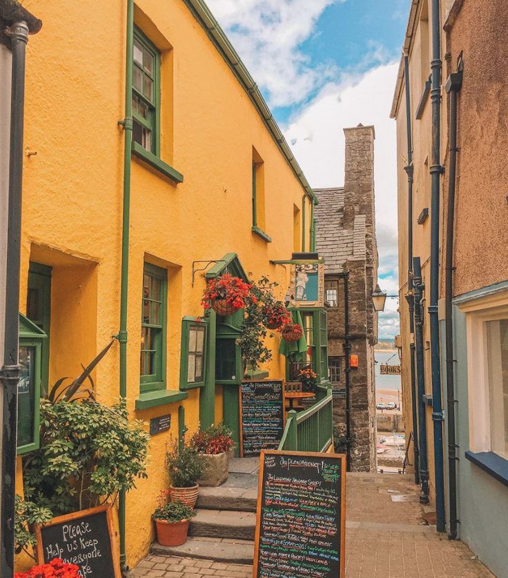 an alley way with yellow buildings and green trim on the side, next to some flowers