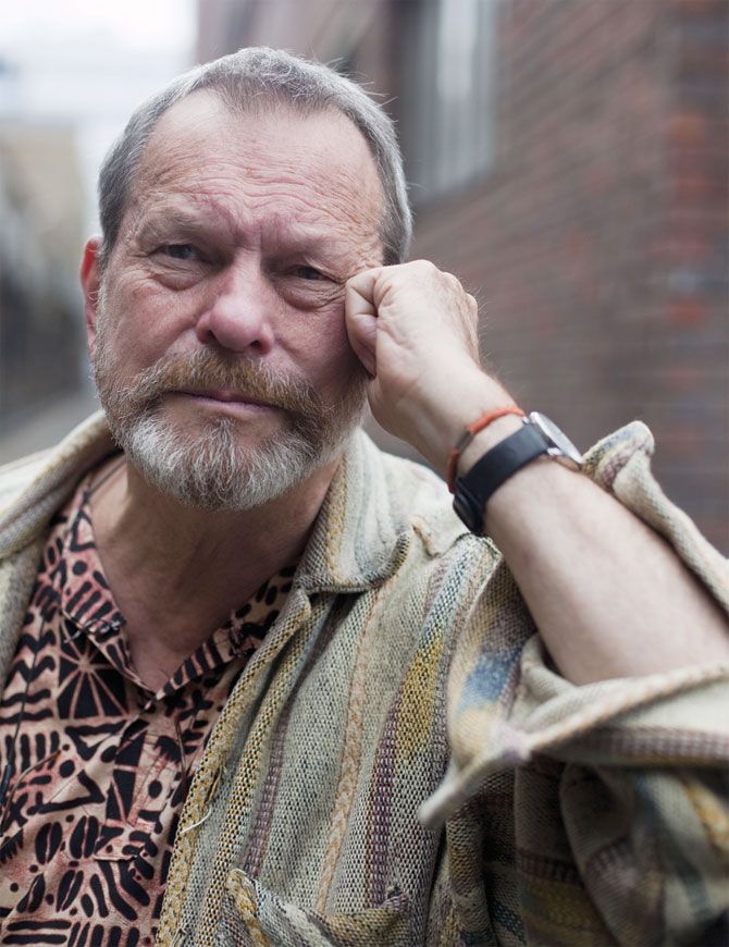 an older man with a white beard wearing a patterned shirt and holding his hand to his ear