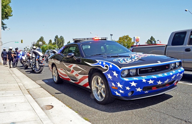 a car painted with stars and stripes on the hood is parked in front of a line of motorcyclists