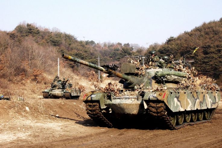 tanks are lined up in the dirt near some trees and bushes on a hill side