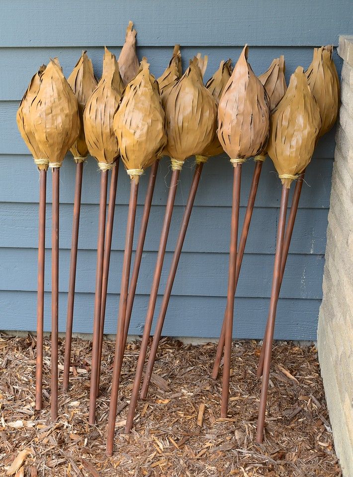 seven wooden flowers are lined up against a blue wall in front of a house with mulch on the ground