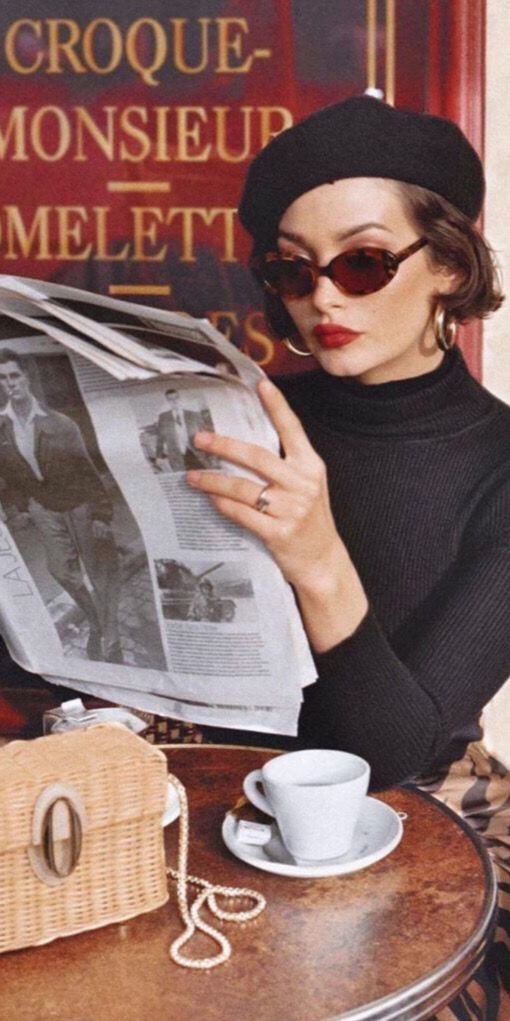 a woman sitting at a table with a newspaper in front of her and a cup of coffee