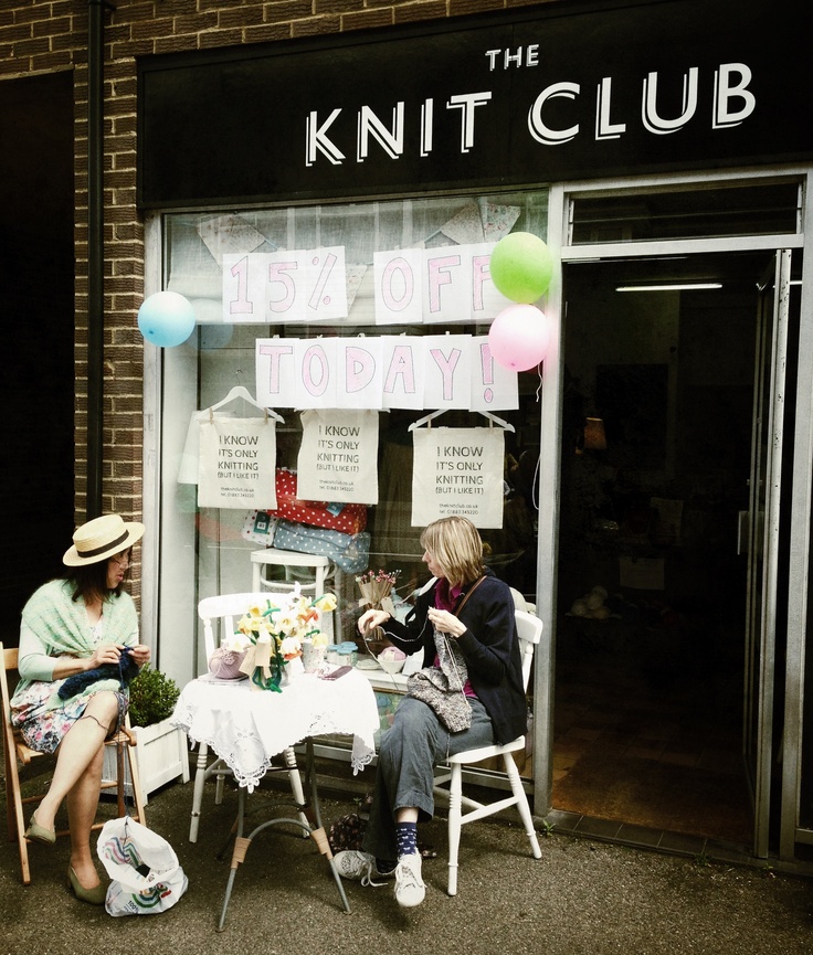 two women sitting at a table in front of a knit club store with balloons on the windows