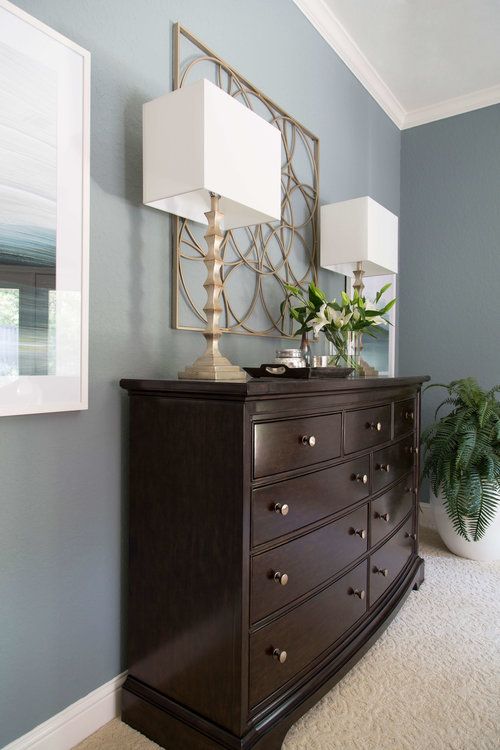 a dresser with two lamps on top and a mirror above it in a room that has blue walls