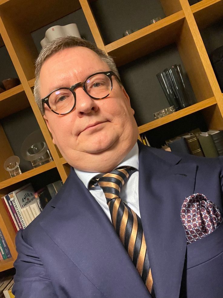 a man in a suit and tie posing for the camera with bookshelves behind him