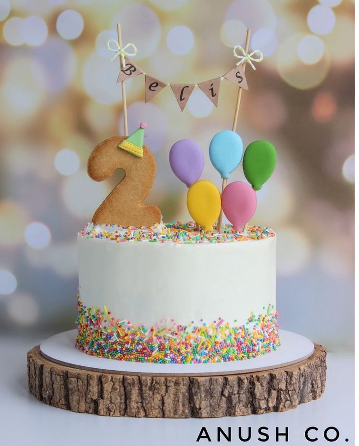 a birthday cake with sprinkles and balloons on top is displayed in front of a blurry background