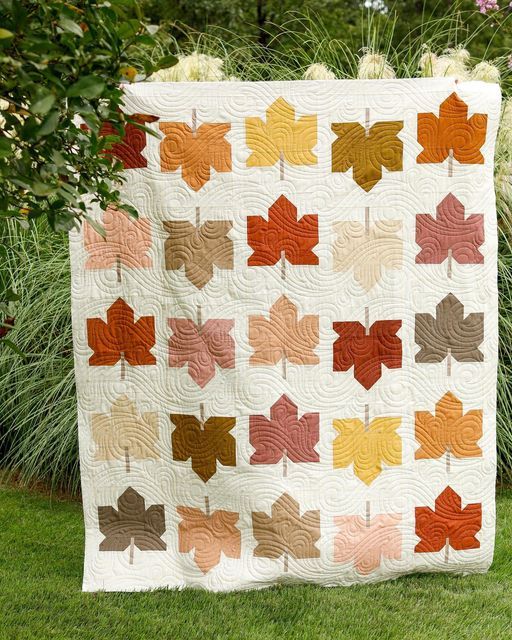 a quilt made with leaves on the grass in front of some bushes and flowers,