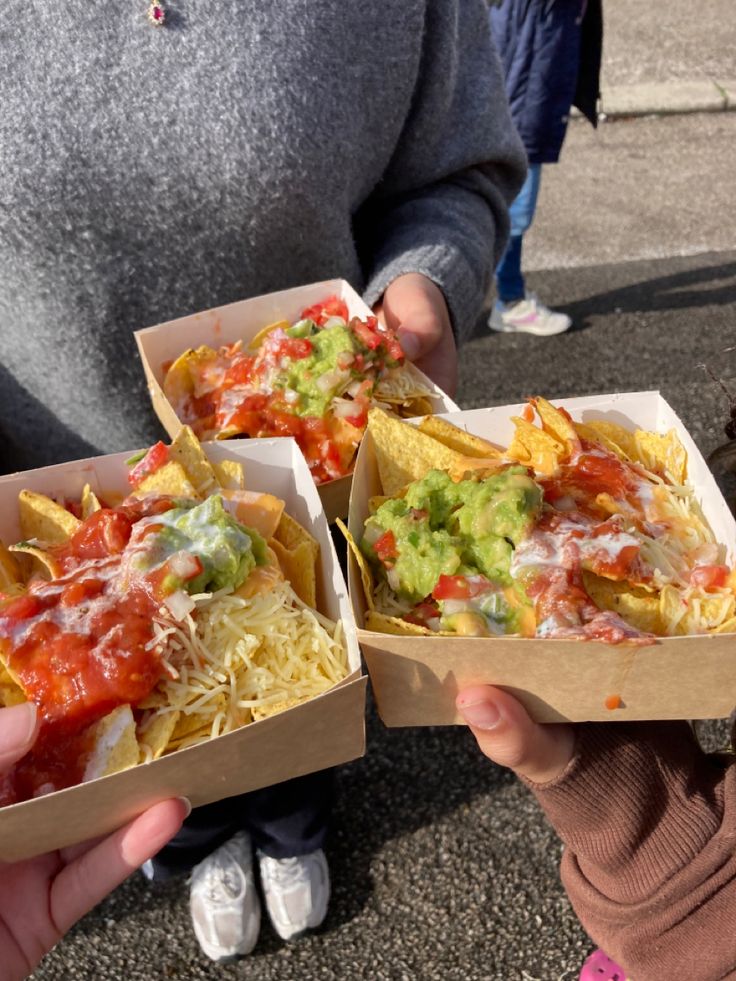 two people holding up boxes of nachos with toppings and chips in them