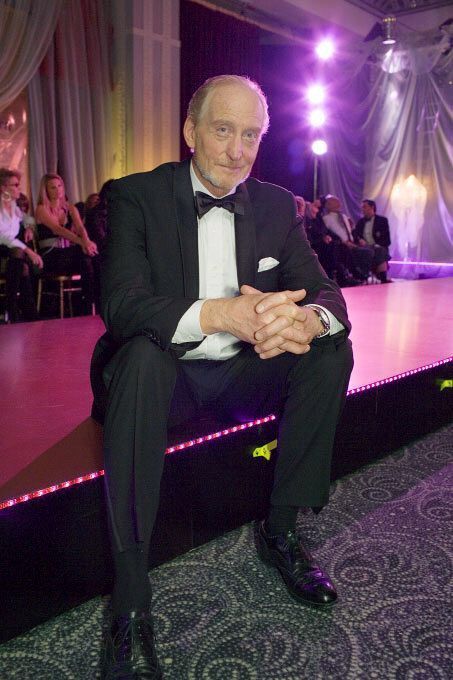 an older man in a tuxedo sitting on a stage at a formal event