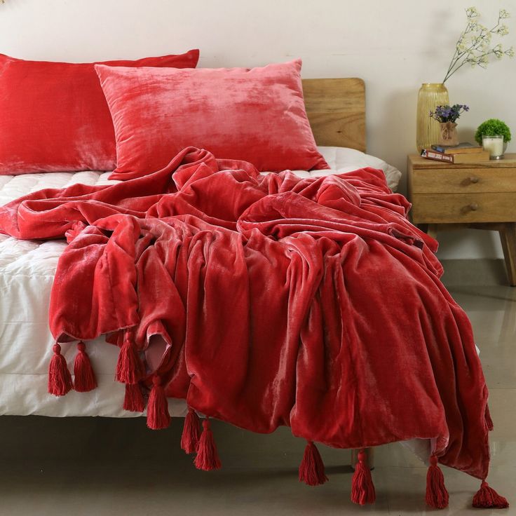 a bed covered in red blankets and pillows with tassels on the headboard