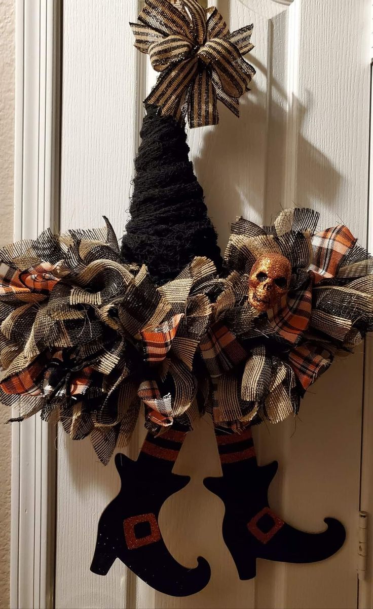 a halloween wreath hanging on the front door with a skull and boots attached to it