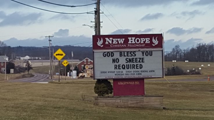 a sign that is in the middle of a field with power lines and buildings behind it