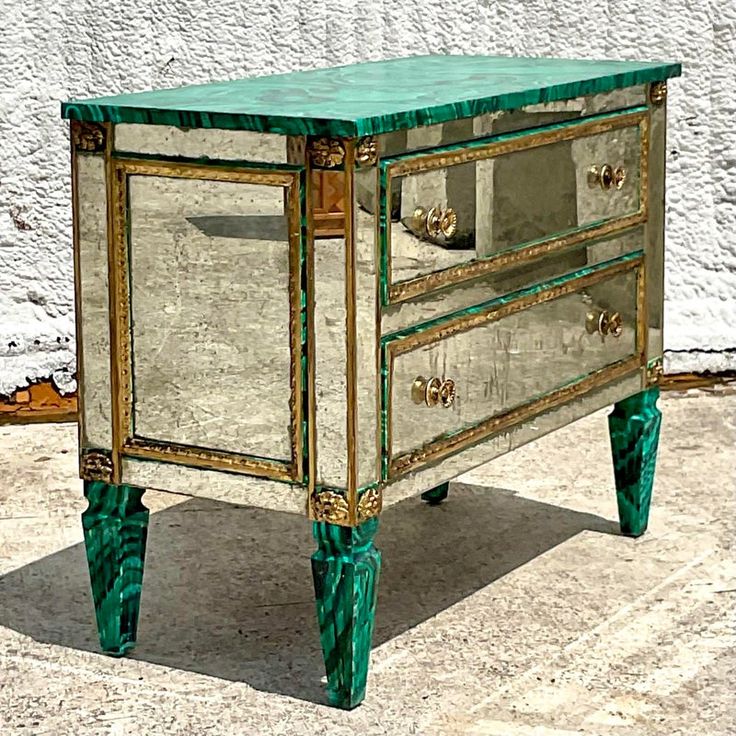 a green and gold mirrored dresser sitting on top of a cement floor next to a white wall