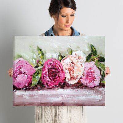 a woman holding up a painting with pink flowers on it