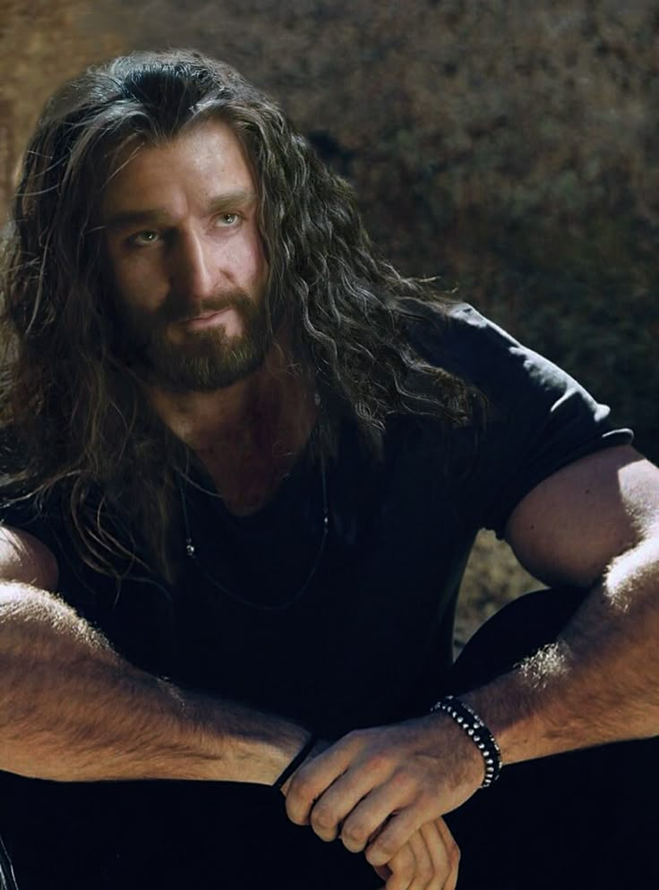 a man with long hair sitting on the ground