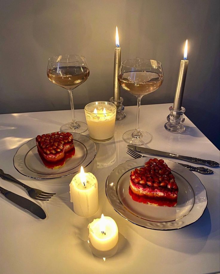 the table is set with two desserts and three glasses of wine, candles, and silverware