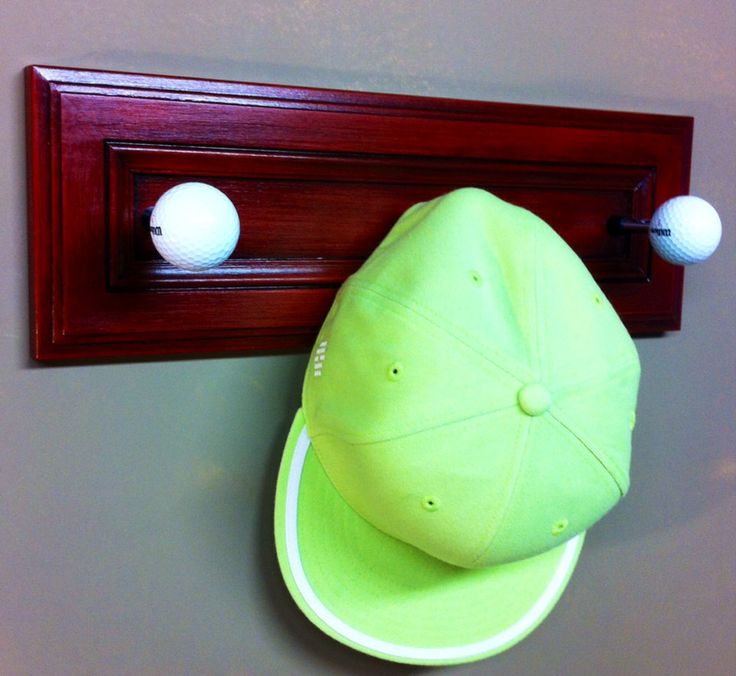 a green hat is hanging on the wall next to a wooden coat rack with two golf balls