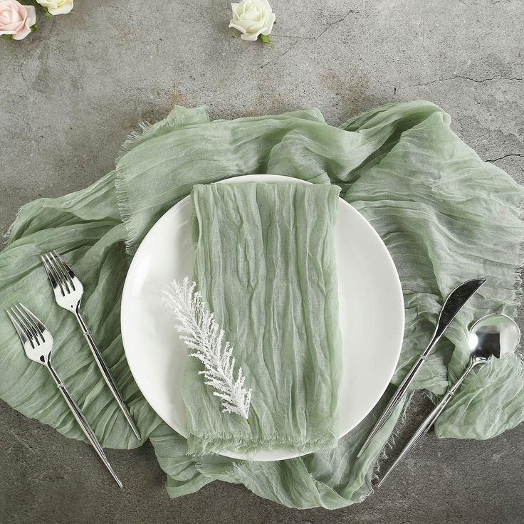 a white plate topped with green napkins next to silverware and flowers on top of a table