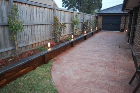 some lights that are on the side of a fence in front of a yard with a brick path