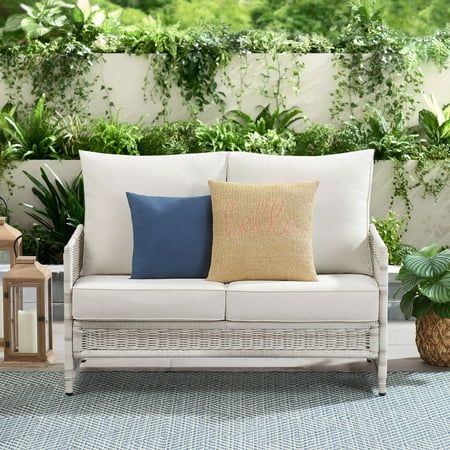 a white couch sitting on top of a blue rug next to a green plant covered wall