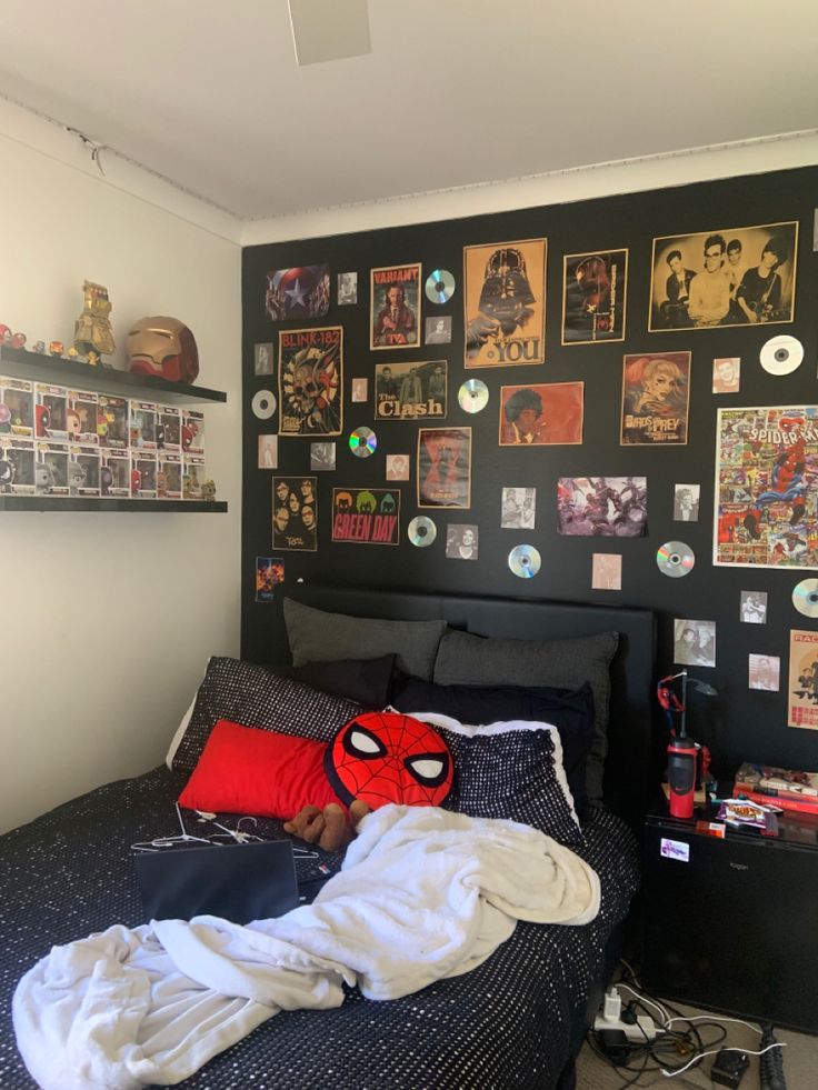 a bedroom with black walls and pictures on the wall above the bed, along with a spiderman pillow