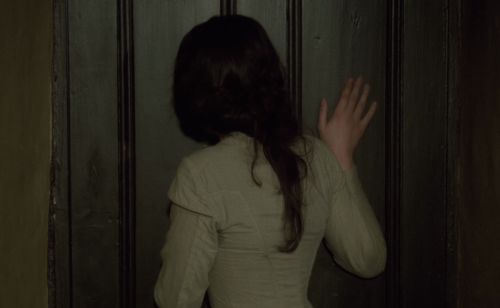 a woman standing in front of a door with her hand on the back of her head