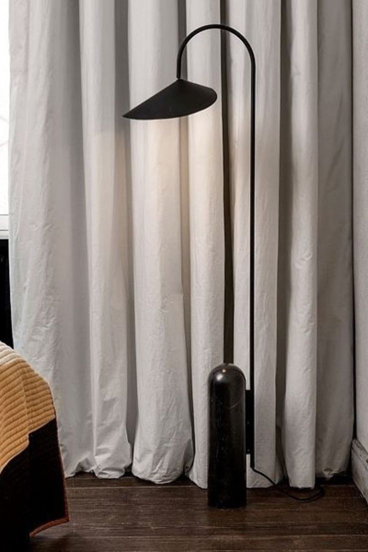 a floor lamp sitting on top of a wooden floor next to a window with white curtains