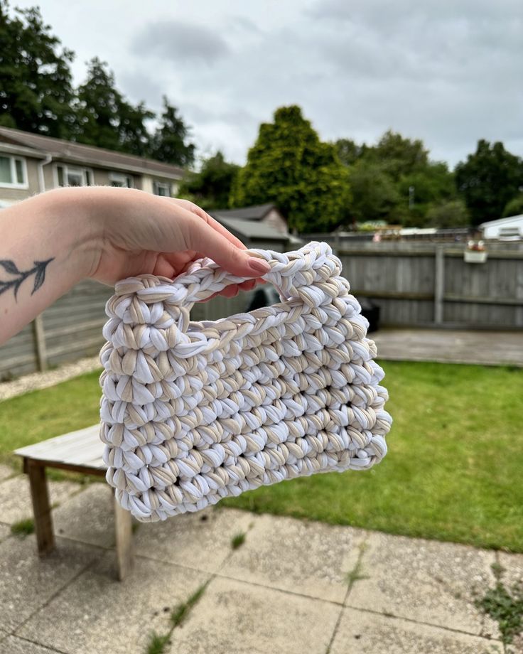 a hand holding a woven purse in front of a house