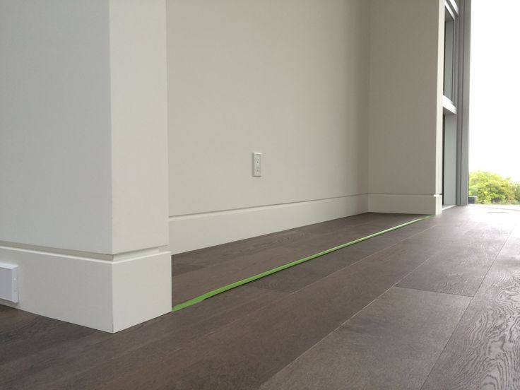 an empty room with white walls and wood flooring in the foreground is a large window