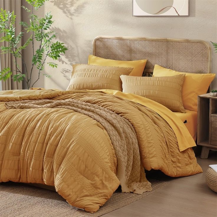 a bed with yellow comforters and pillows in a room next to a plant on the floor