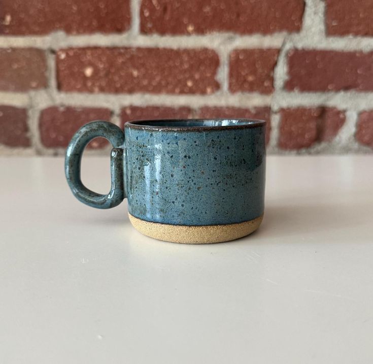 a coffee cup sitting on top of a white table next to a brick wall and floor