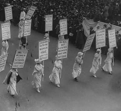 a group of women marching down a street holding signs in front of a large crowd