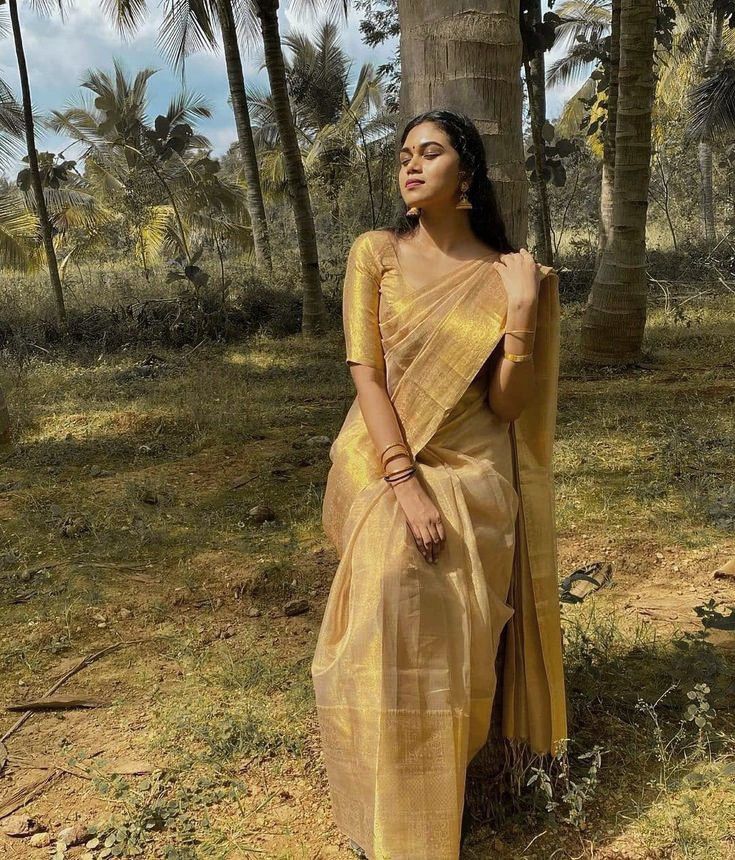 a woman in a yellow sari standing next to a tree