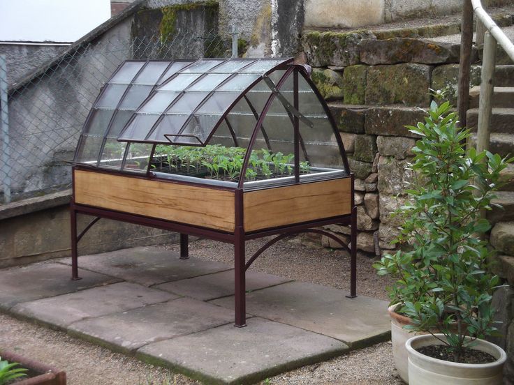 a small greenhouse with plants in it on the side of a stone wall next to a planter