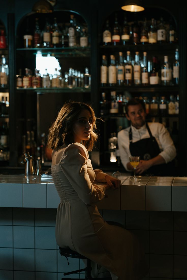 a woman sitting at a bar with a man behind her