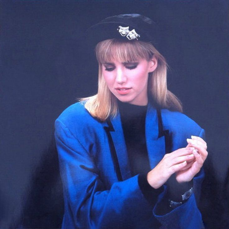 a woman wearing a blue coat and hat looking at her cell phone while standing in front of a black background