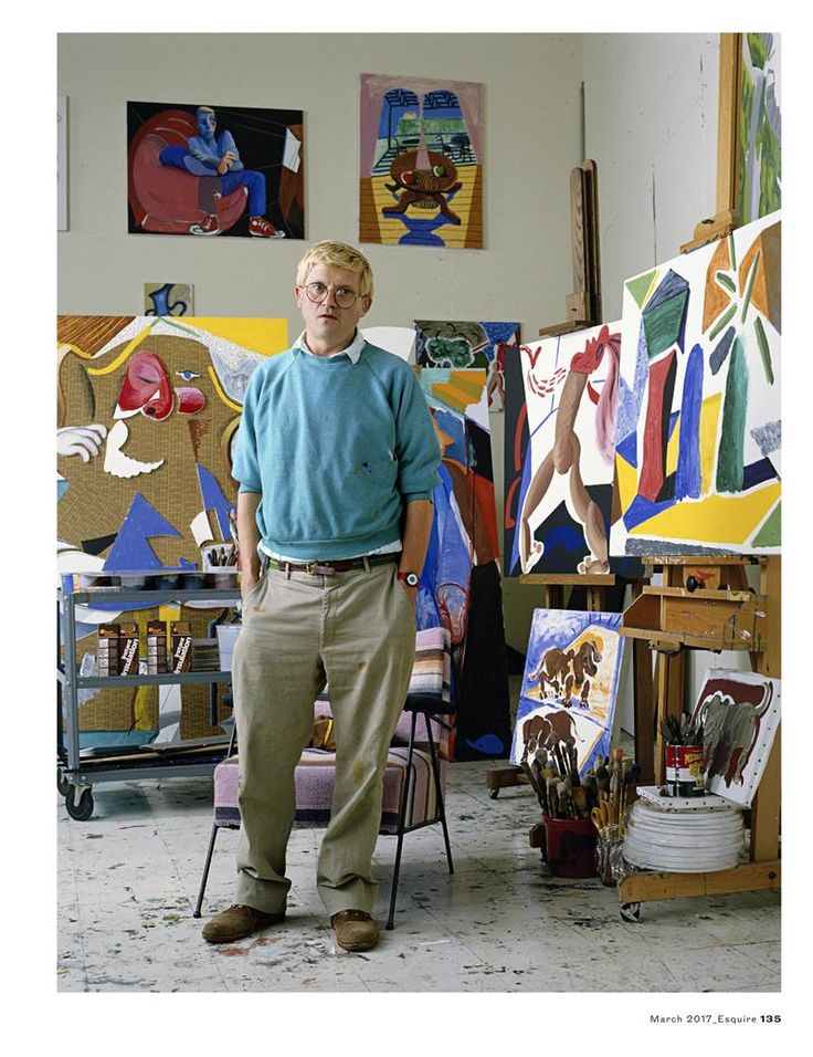 an older man standing in front of paintings on easels and canvases with his hands behind him