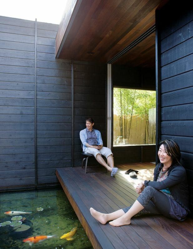 two people sitting on a wooden deck next to a pond with koi fish in it